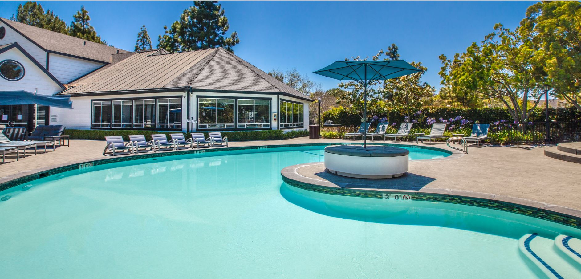 Large pool in front of clubhouse with seating and umbrella